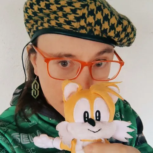 I'm protographed holding that little orange fox buddy while wearing a Sega hoodie. I flatter myself on androgynous looks, look young for my age, have light skin, and most importantly, wear cool S earrings.